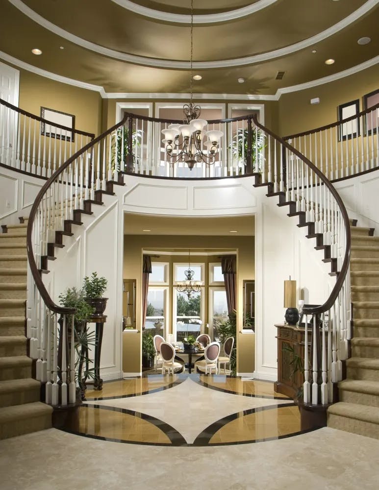 This beautiful entry boasts a luxurious staircase with carpeted steps. The area features gorgeous decorated flooring and a stunning two-story ceiling.